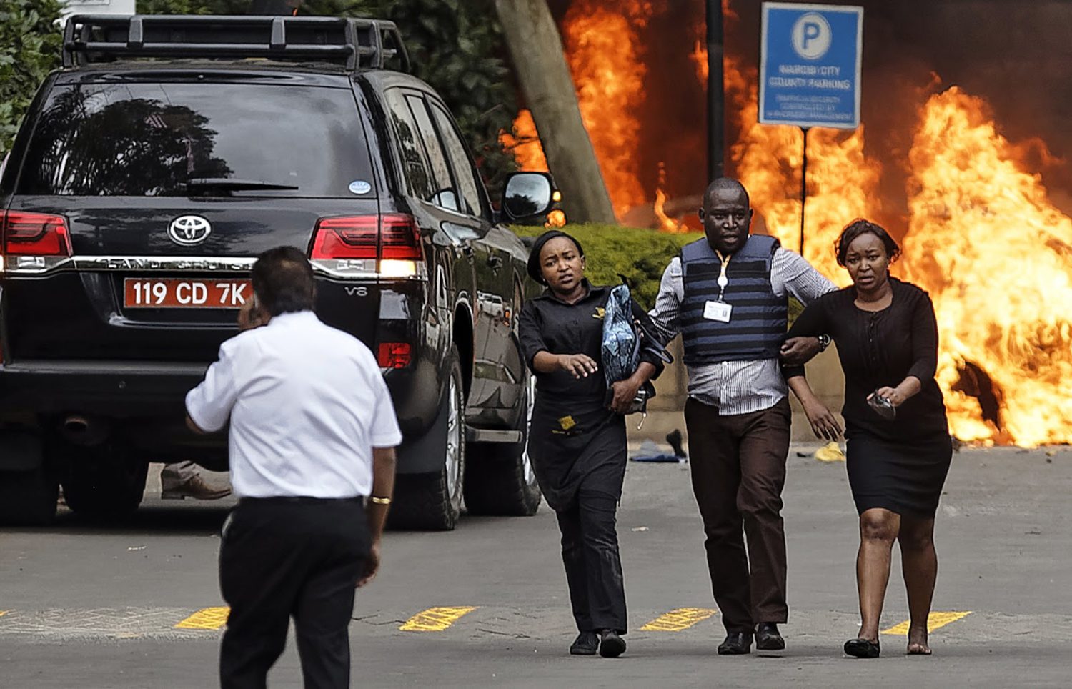 Security forces help civilians flee the scene as cars burn at a hotel complex in Nairobi, Kenya, on Tuesday, Jan. 15. Terrorists attacked an upscale hotel complex in Kenya's capital Tuesday, sending people fleeing in panic as explosions and heavy gunfire reverberated through the neighborhood. (AP Photo/Ben Curtis)