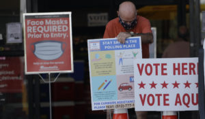 An election worker wearing a mask for protection against COVID-19 adjust signs for an early polling site located at a grocery store, Thursday, July 9, 2020, in Austin, Texas. (AP Photo/Eric Gay)