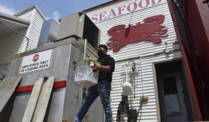 In this image for the Howard Center for Investigative Journalism at the University of Maryland's Philip Merrill College of Journalism, a Lindy's worker carries crabs and corn onto a loading dock April 21, 2021, in the company's Woolford, Maryland, location. The company on Chesapeake Bay hires local and migrant workers to process live crabs, crab meat and oysters. (Carmen Molina Acosta/University of Maryland via AP)