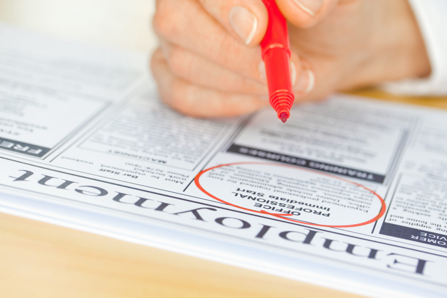 A hand with a pen circling a job in the paper (focus on pen nib and ad)