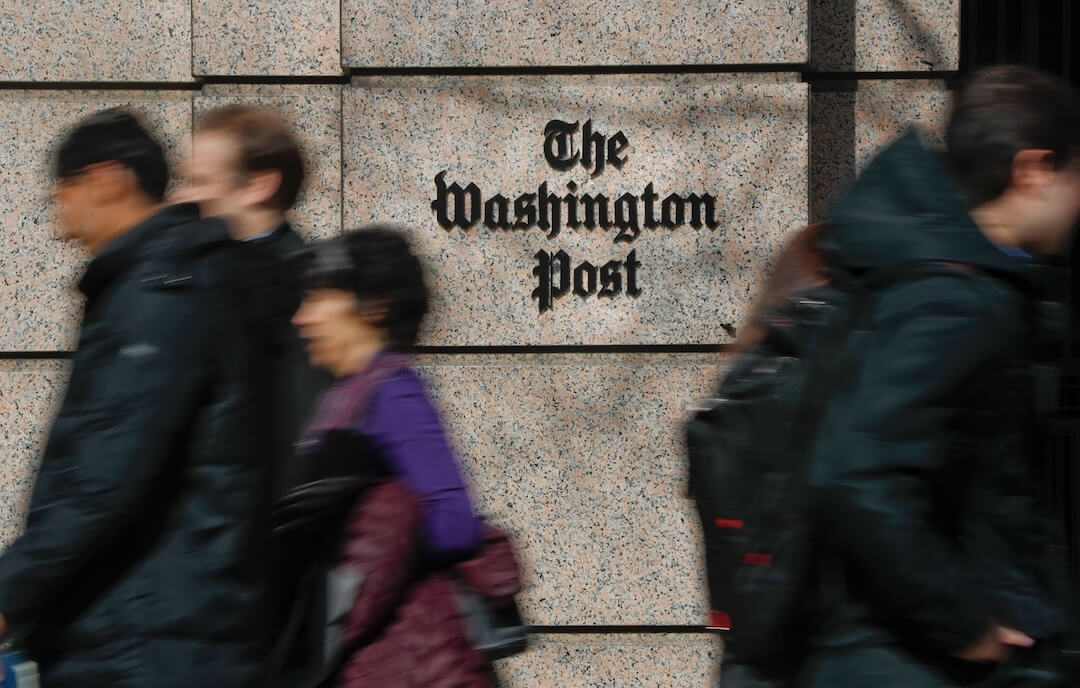 People walk by a sign at the Washington Post building