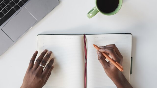 Minimal top view of unrecognizable African-American woman writing in planner at white business workplace