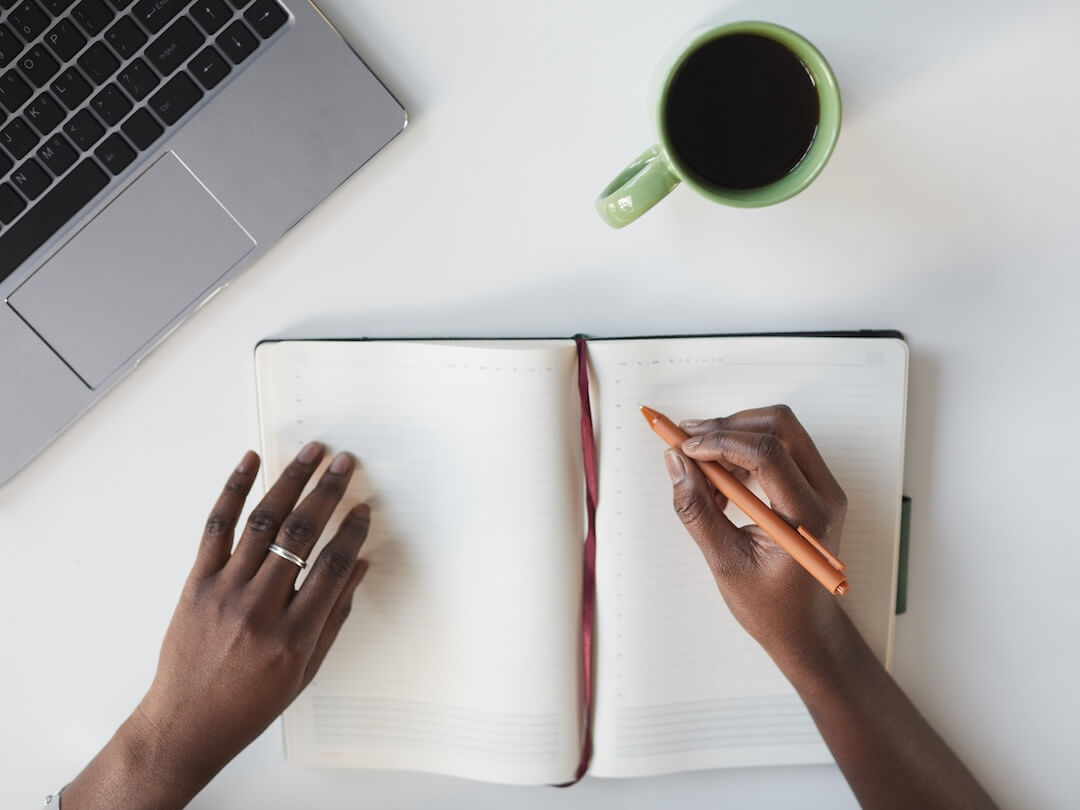Minimal top view of unrecognizable African-American woman writing in planner at white business workplace
